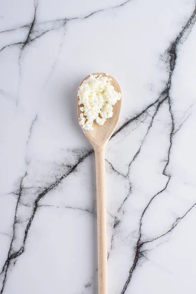 Top view of wooden spoon with fresh cottage cheese on marble surface — Stock Photo