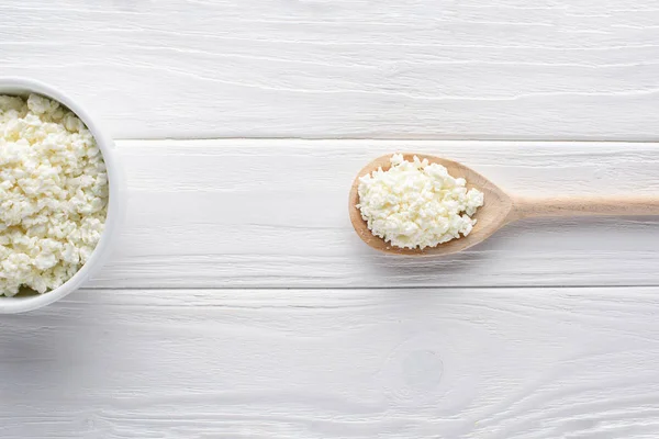 Top view of fresh healthy cottage cheese in bowl and wooden spoon on table — Stock Photo