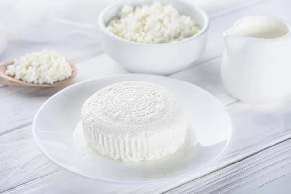 Fresh cottage cheese, wooden spoon and milk in jug on wooden table — Stock Photo