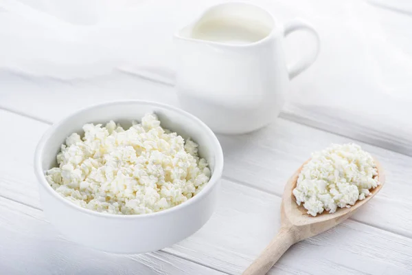 Close-up view of fresh healthy cottage cheese, wooden spoon and milk in jug on wooden table — Stock Photo