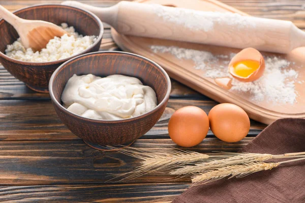 Vue rapprochée du fromage cottage, des épis de blé, de la crème sure, des œufs et de la farine sur une table en bois — Photo de stock