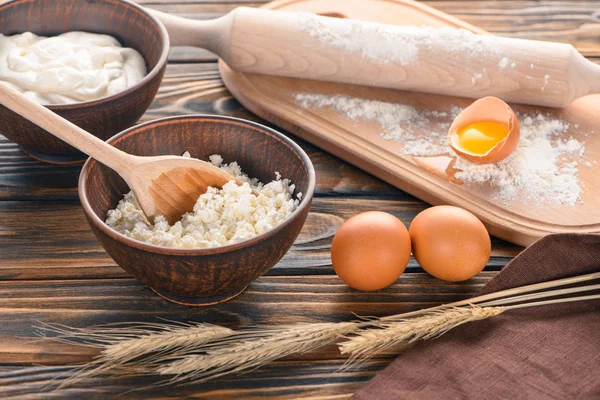 Fresh cottage cheese, wheat ears, sour cream, eggs and flour on wooden table — Stock Photo