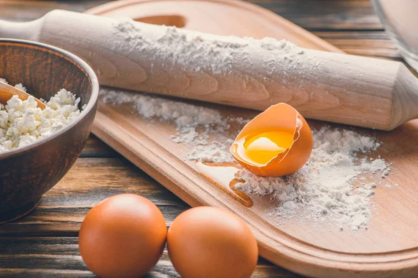 Close-up view of raw eggs, flour with rolling pin and cottage cheese on wooden table — Stock Photo