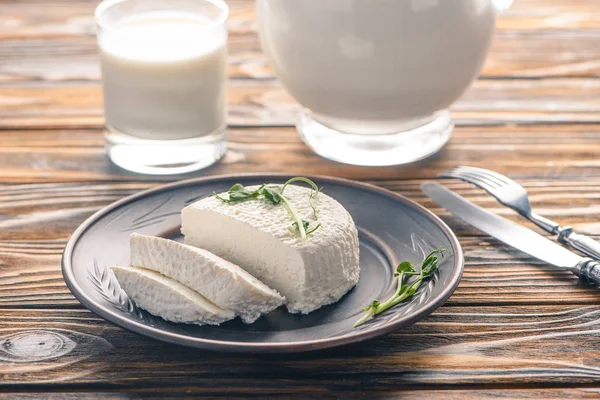 Крупный план вкусного здорового мягкого сыра на тарелке и стакан молока на деревянном столе — стоковое фото