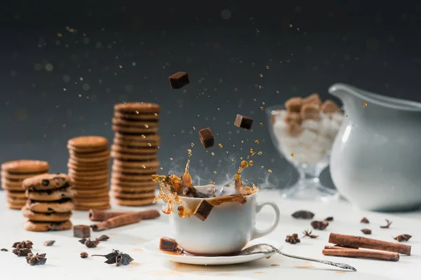 Zucchero di canna cubetti spruzzando in tazza con caffè nero caldo di fronte a biscotti e spezie — Foto stock