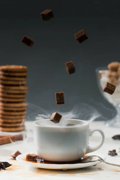 Steaming coffee cup with falling cane sugar cubes by cookies on table — Stock Photo