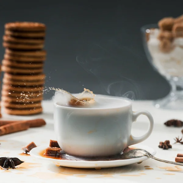 Cubos de açúcar mascavo salpicando em xícara de café na mesa com biscoitos e especiarias — Fotografia de Stock
