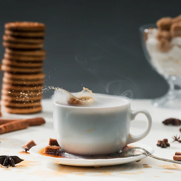 Cubes de sucre brun éclaboussant dans une tasse de café sur la table avec des biscuits et des épices — Photo de stock