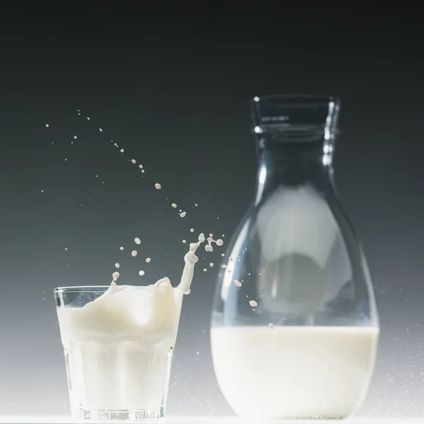 Glass of milk with splashes in front of milk bottle — Stock Photo