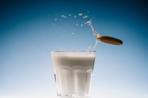 Biscotti Cracker spruzzando nel bicchiere di latte su sfondo blu — Foto stock