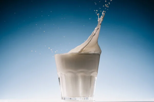 Leite fluindo em vidro de leite no fundo azul — Fotografia de Stock