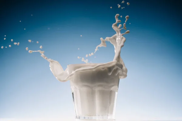 Glas Milch mit großen Spritzern isoliert auf blauem Hintergrund — Stockfoto