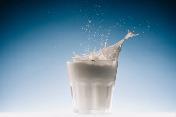 Vetro con latte e spruzzi isolati su sfondo blu — Foto stock