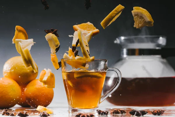 Glass cup of hot steaming tea with falling citrus pieces — Stock Photo