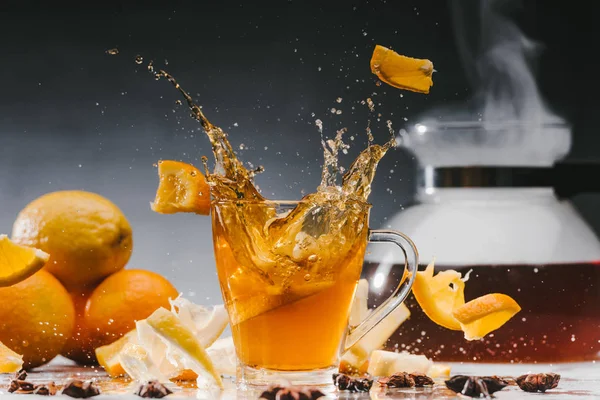 Grandes éclaboussures de thé dans une tasse en verre avec des agrumes et des épices — Photo de stock