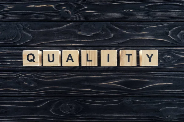 Top view of word quality made of wooden blocks on dark wooden tabletop — Stock Photo