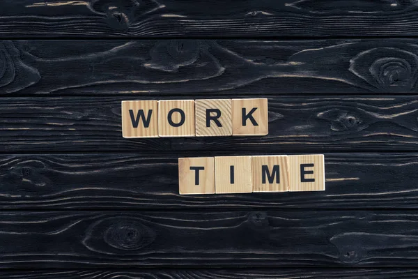 Vue de dessus des mots de temps de travail faits de blocs de bois sur dessus de table en bois foncé — Photo de stock