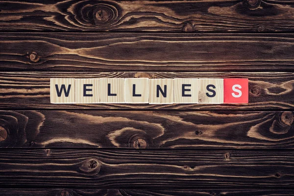 Top view of wooden blocks arranged in wellness word in brown wooden surface — Stock Photo