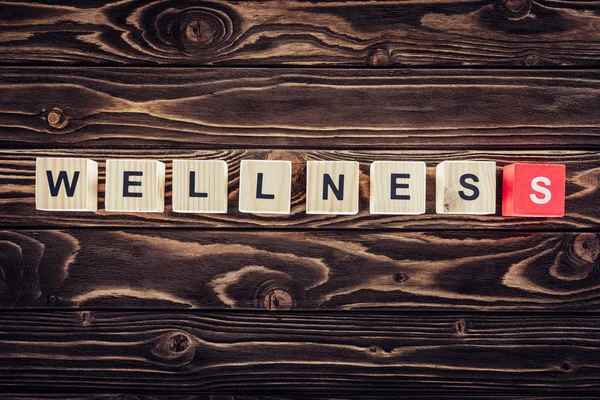 Top view of wooden blocks arranged in wellness word in brown wooden surface — Stock Photo