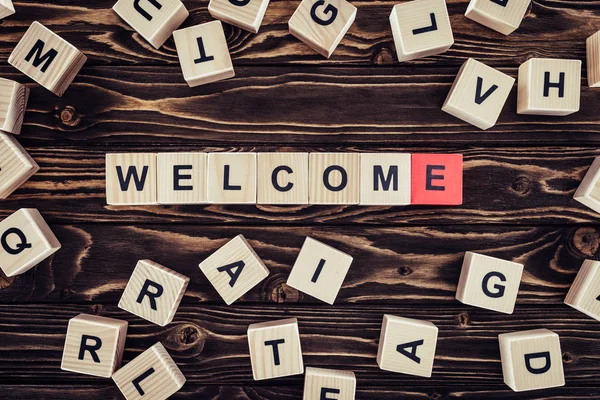 Flat lay with wooden cubes arranged in welcome word on brown wooden surface — Stock Photo