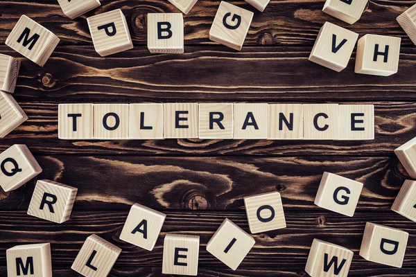 Flat lay with arranged wooden blocks in tolerance word on brown wooden surface — Stock Photo