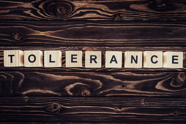 Flat lay with arranged wooden blocks in tolerance word on brown wooden surface — Stock Photo