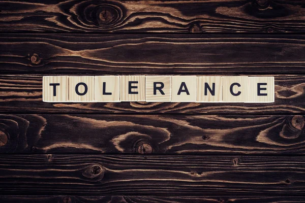 Flat lay with arranged wooden blocks in tolerance word on brown wooden surface — Stock Photo