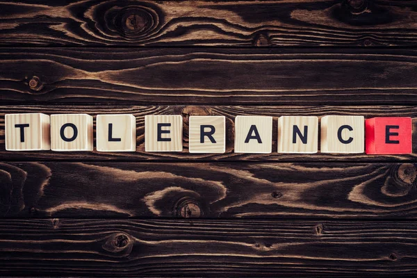 Flat lay with arranged wooden blocks in tolerance word on brown wooden surface — Stock Photo