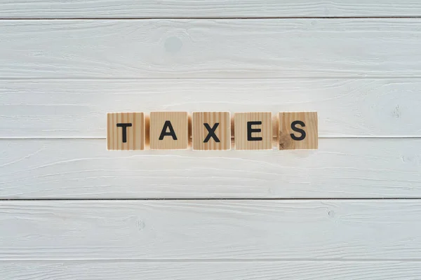 Top view of wooden blocks arranged in taxes word on white wooden tabletop — Stock Photo