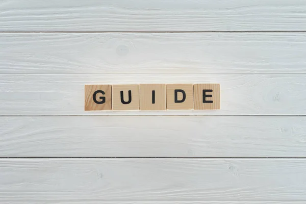 Vue du dessus du mot guide fait de blocs de bois sur une surface en bois blanc — Photo de stock