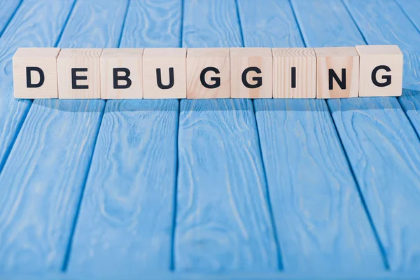 Close up view of debugging word made of wooden blocks on blue tabletop — Stock Photo