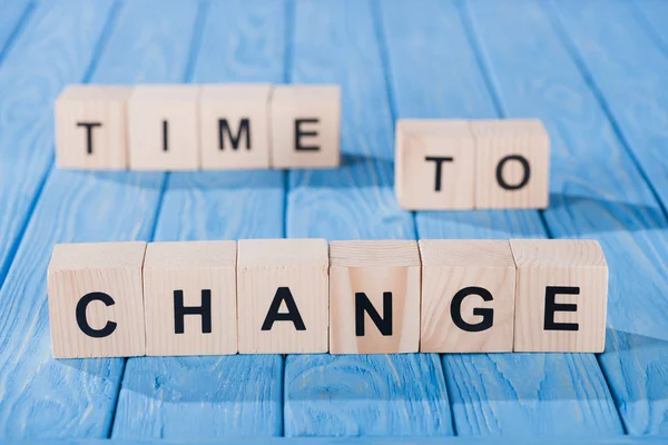 Close up view of arranged wooden blocks into time to change phrase on blue wooden surface — Stock Photo