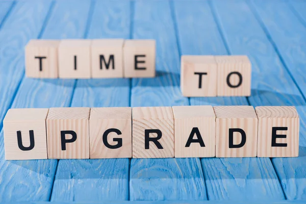 Close up view of arranged wooden blocks into time to upgrade phrase on blue wooden surface — Stock Photo