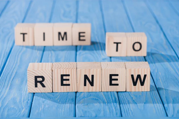 Close up view of arranged wooden blocks into time to renew phrase on blue wooden surface — Stock Photo