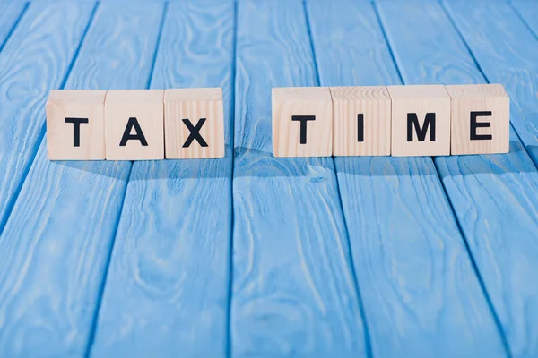 Close up view of arranged wooden blocks into tax time phrase on blue wooden surface — Stock Photo