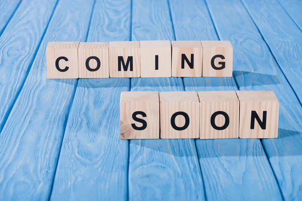 Close up view of arranged wooden blocks into coming soon phrase on blue wooden surface — Stock Photo