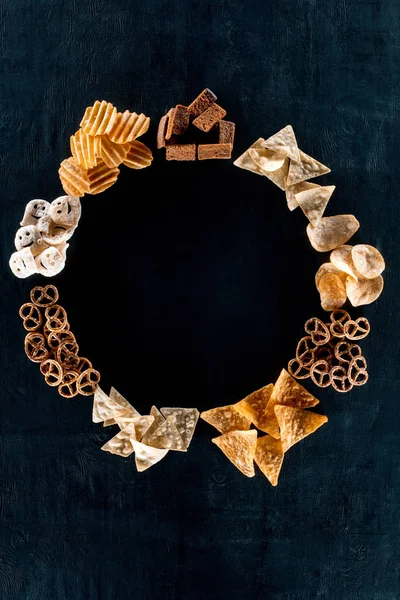 Top view of round frame made from various unhealthy snacks on black — Stock Photo