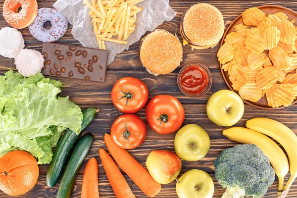 Top view of fresh fruits with vegetables and assorted unhealthy food on wooden table — Stock Photo