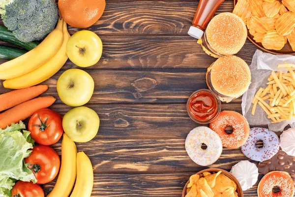 Верхний вид свежих спелых фруктов с овощами и разнообразной нездоровой пищи на деревянный стол — стоковое фото