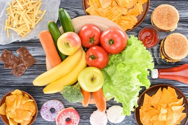 Vista superior de una variedad de comida chatarra y frutas frescas con verduras en la mesa de madera - foto de stock