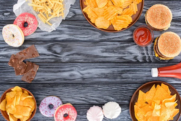 Вид зверху асортиментованої нездорової їжі та цукерок на дерев'яному столі — стокове фото