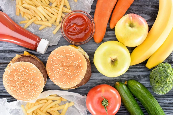 Vista superior de frutas frescas com legumes e junk food na mesa de madeira — Fotografia de Stock