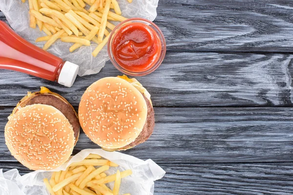 Vista superior de hamburguesas con papas fritas y ketchup en mesa de madera - foto de stock