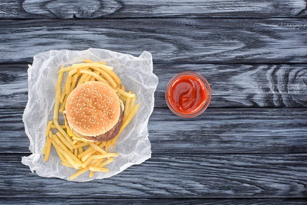 Vista superior de la hamburguesa con papas fritas y ketchup en la mesa de madera - foto de stock