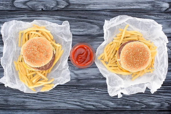 Vista superior de hamburguesas con papas fritas y ketchup en mesa de madera - foto de stock