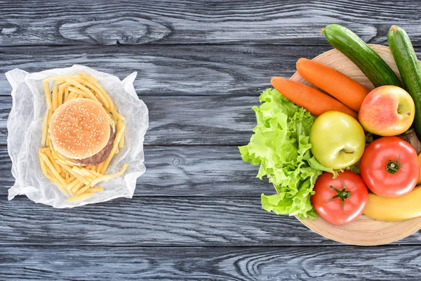 Top view of hamburger with french fries and fresh fruits with vegetables on wooden table — Stock Photo