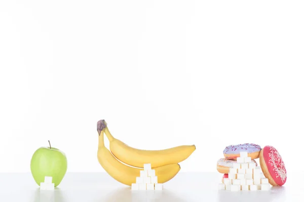 Pommes, bananes et beignets avec des cubes de sucre sur blanc — Photo de stock