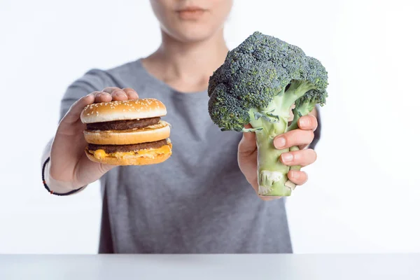 Vue rapprochée de la femme tenant un brocoli frais mûr et un hamburger — Photo de stock