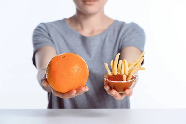 Cropped shot of girl holding ripe orange and ketchup with french fries — Stock Photo