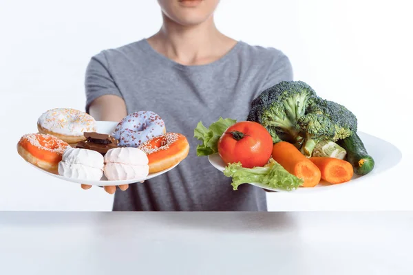 Cropped shot of woman holding plates with sweets and vegetables — Stock Photo